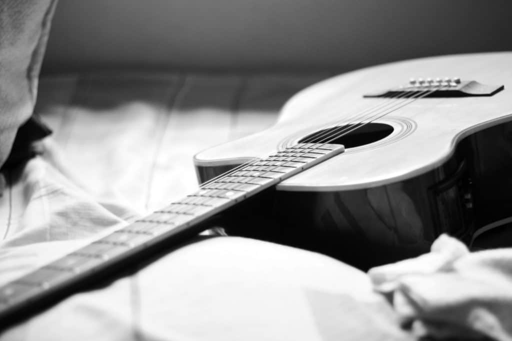 gray-scale-photography-of-acoustic-guitar-on-bed-725469